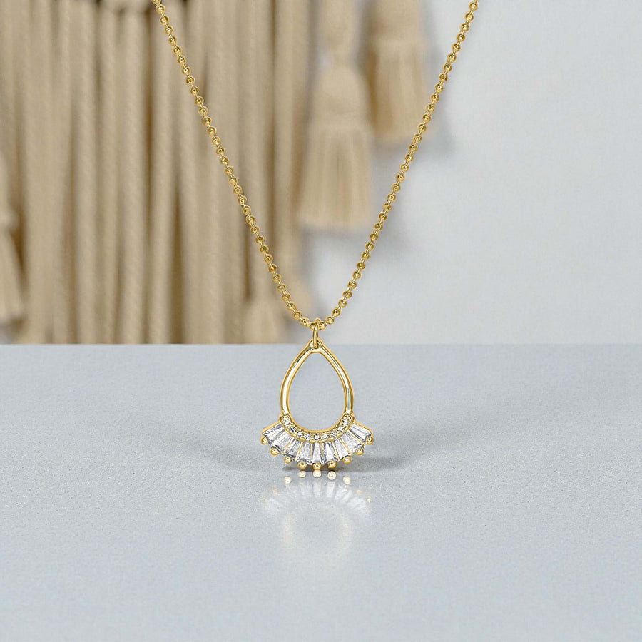 Gold necklace with a teardrop-shaped pendant on a light gray surface.
